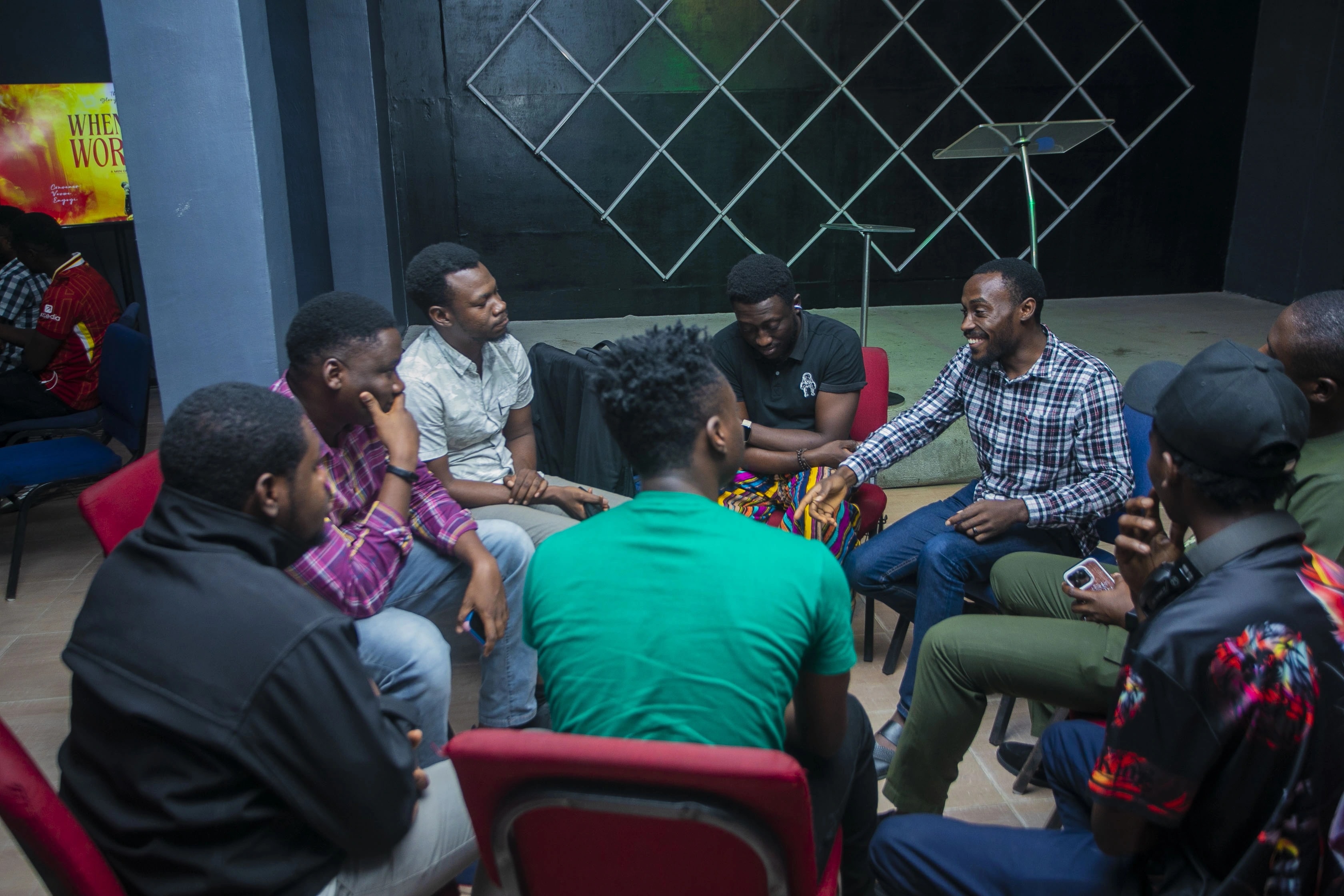 Men seated in a close circle, one speaking while the others listen